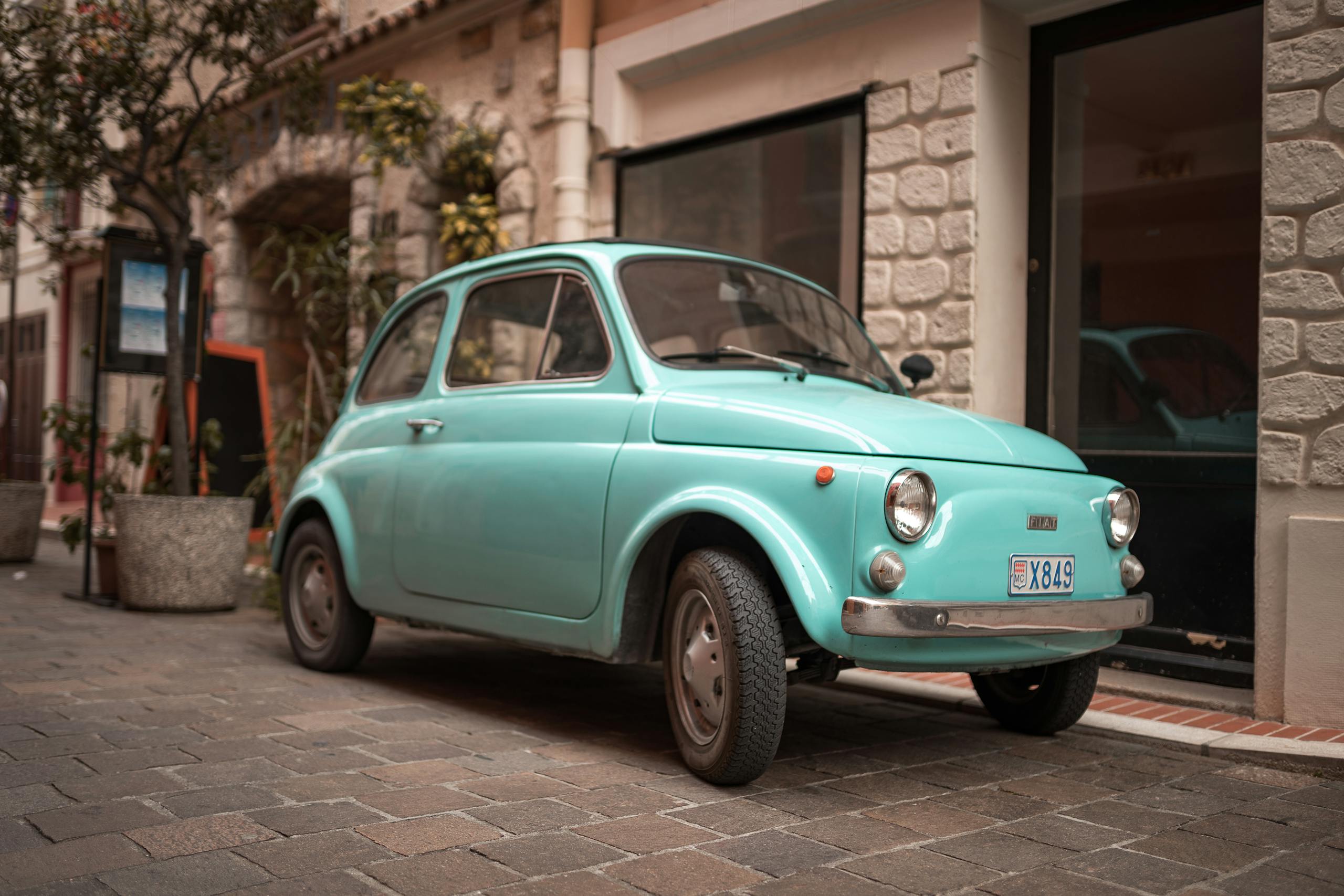 A classic vintage Fiat car parked on a cobblestone street in a quaint European neighborhood.