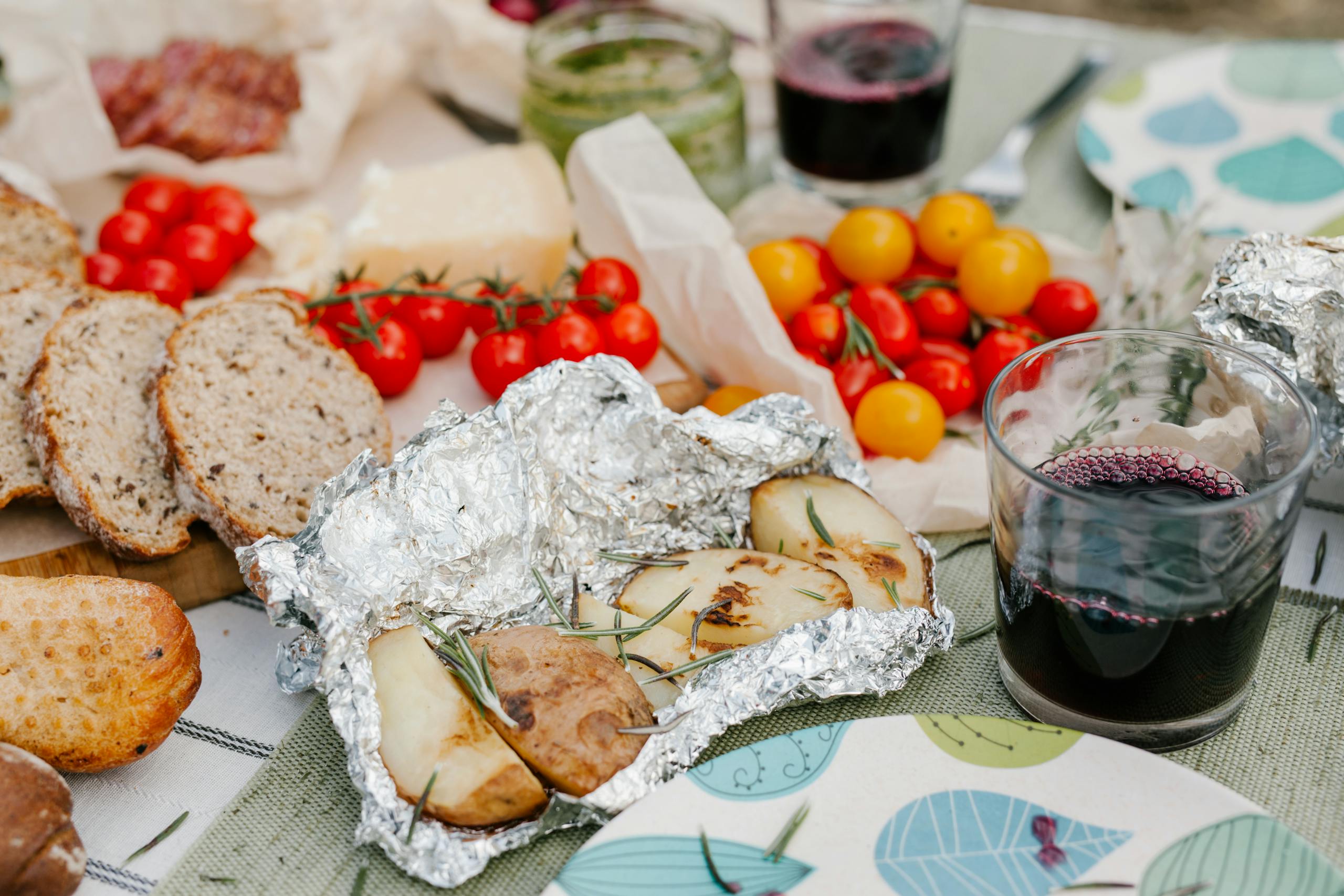 Enjoy a rustic Italian picnic with bread, tomatoes, roasted potatoes, and wine. Perfect for outdoor dining lovers.